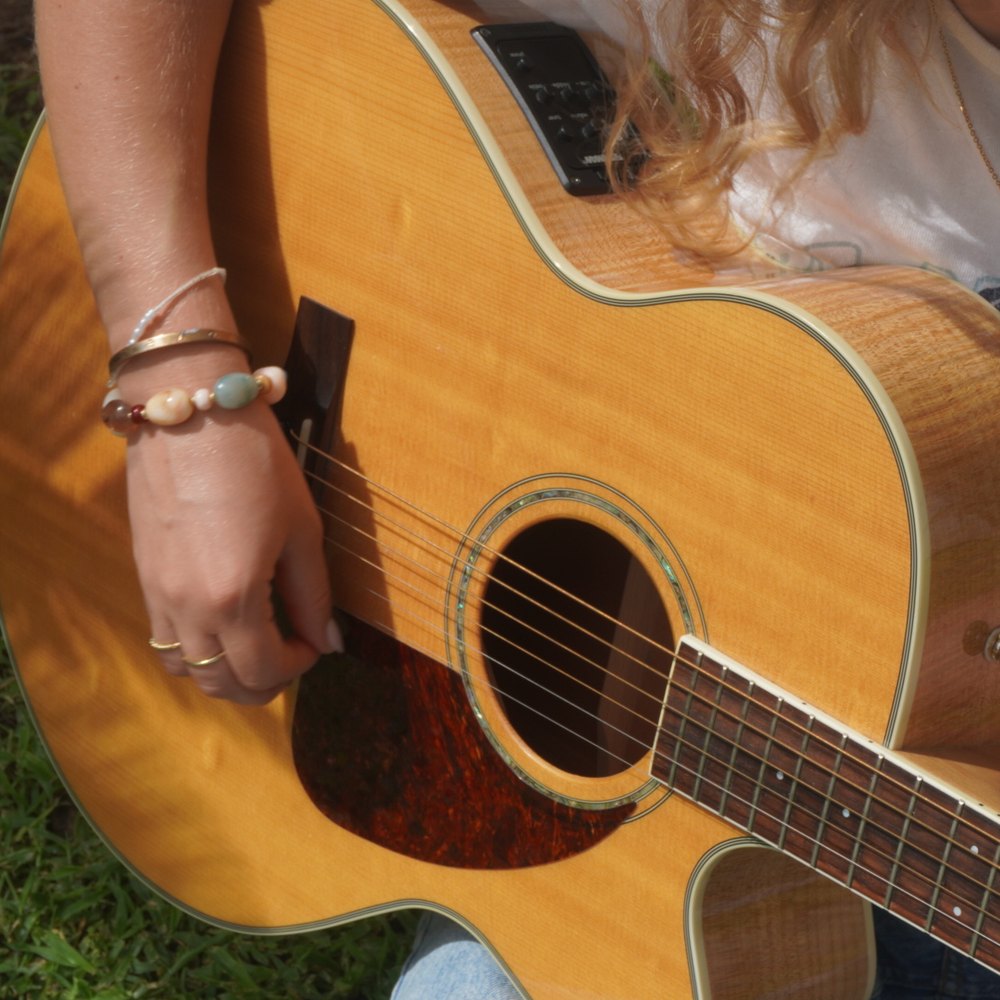 A hand in beaded bracelets strumming an acoustic guitar